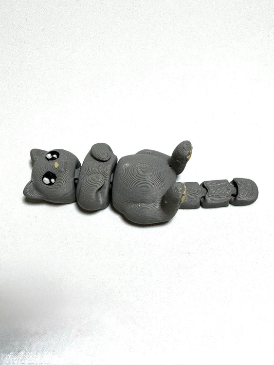 Mochi the Cat Flexling toy in black, lying on back with paws up in relaxed belly-up pose