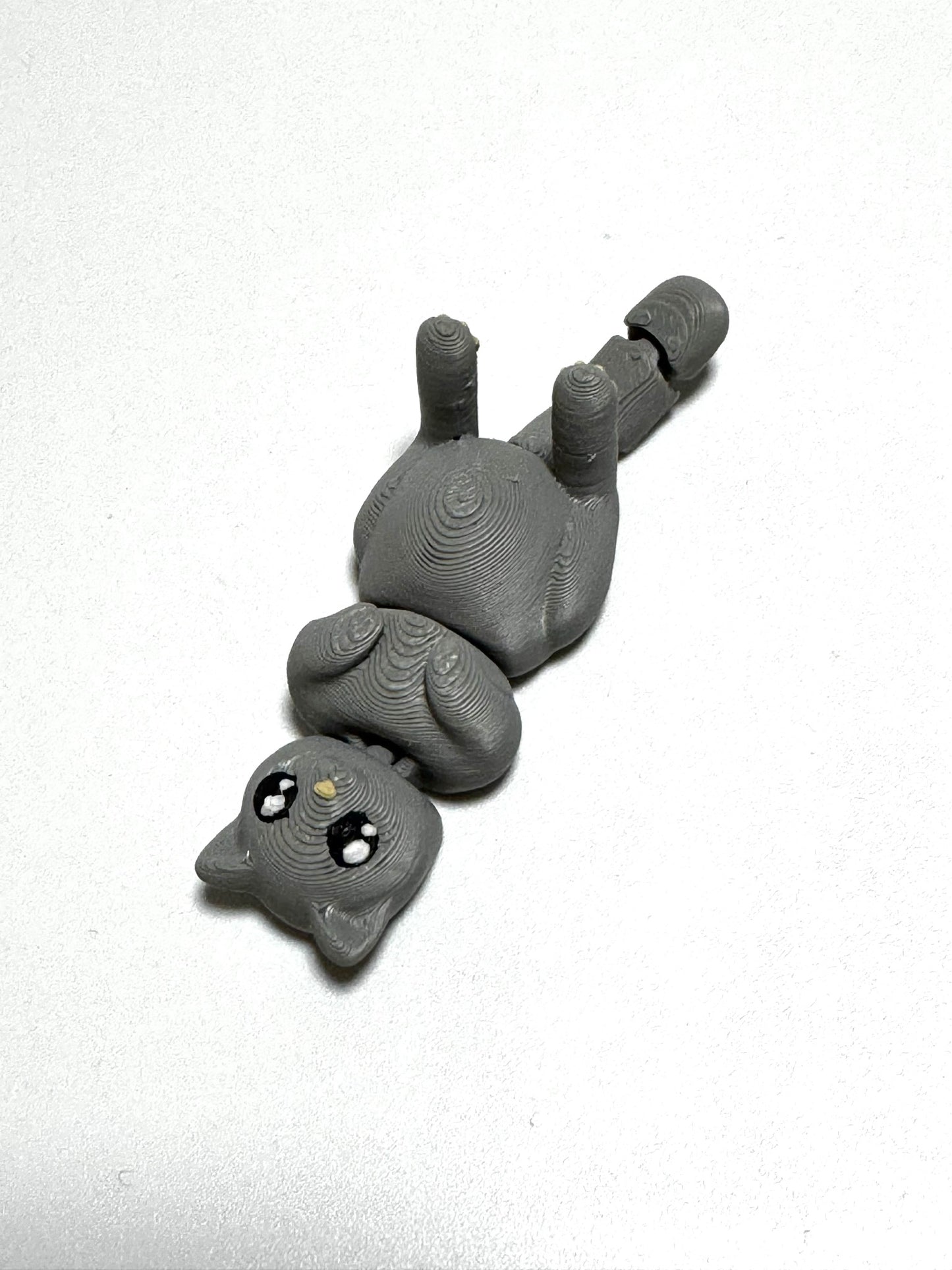 Mochi the Cat Flexling toy in black, lying on back with paws up in relaxed belly-up pose