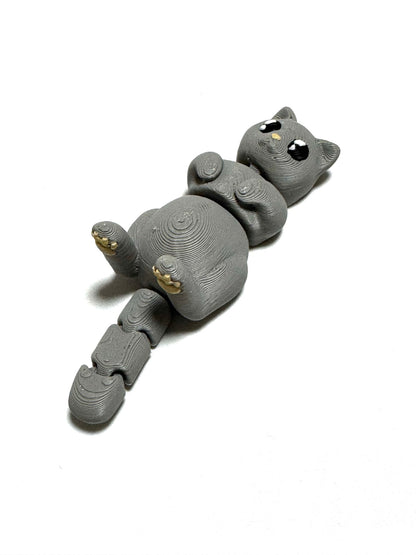 Mochi the Cat Flexling toy in black, lying on back with paws up in relaxed belly-up pose