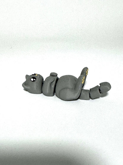 Mochi the Cat Flexling toy in black, lying on back with paws up in relaxed belly-up pose