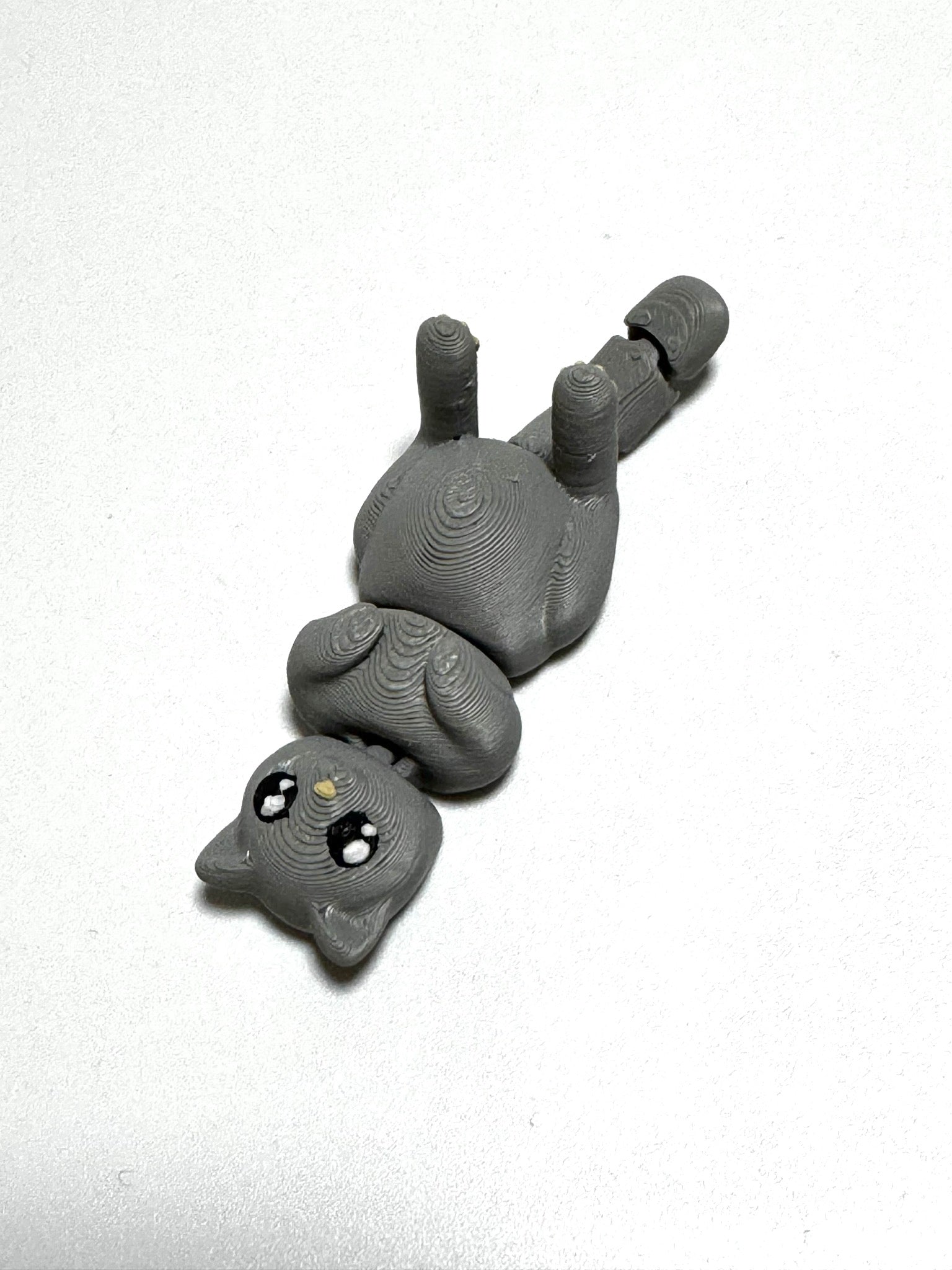 Mochi the Cat Flexling toy in black, lying on back with paws up in relaxed belly-up pose